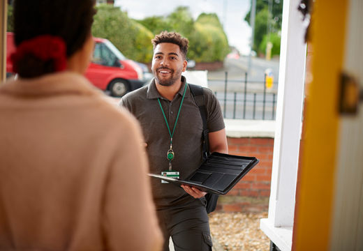 A professional with a lanyard and clipboard smiling at a resident's front door.