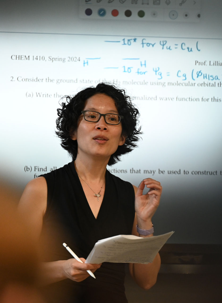 A professor teaching a chemistry class in front of a projected exam slide.
