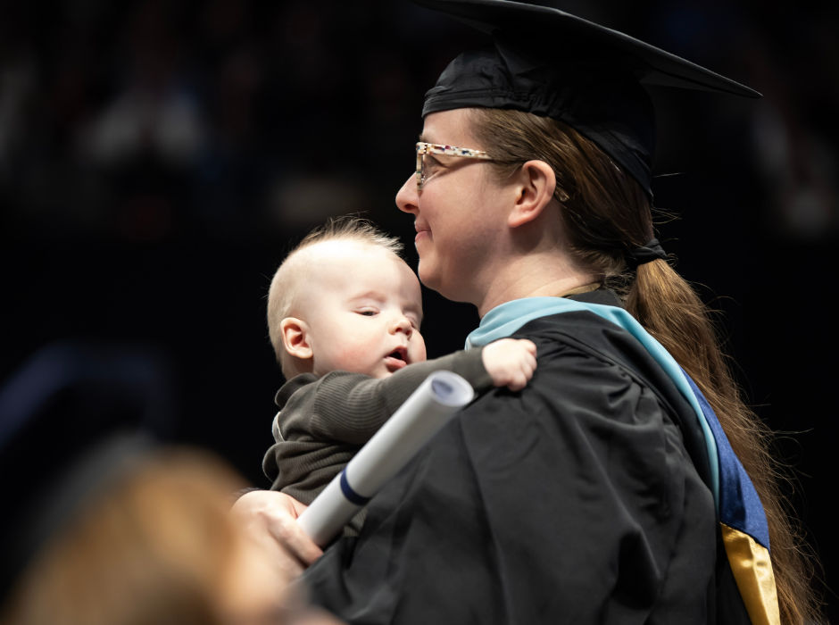 A graduate holding her baby and diploma at commencement.