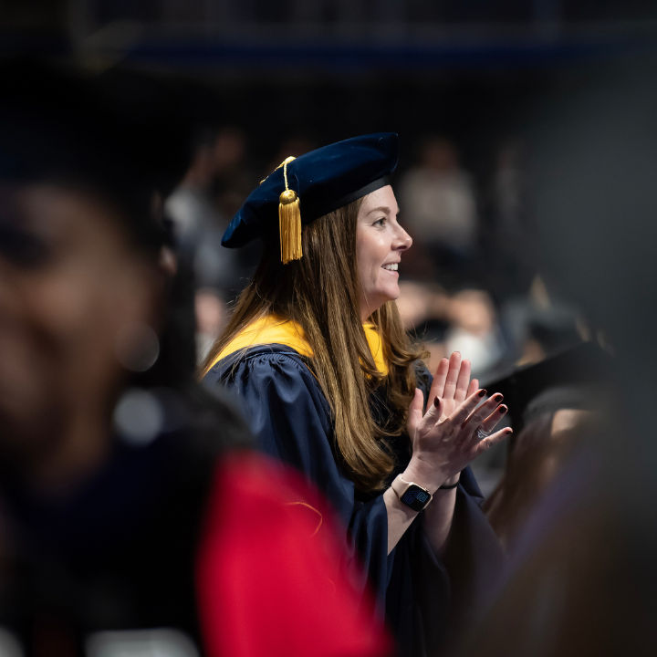 A woman smiling and clapping at a graduation ceremony for University of Pittsburgh students.