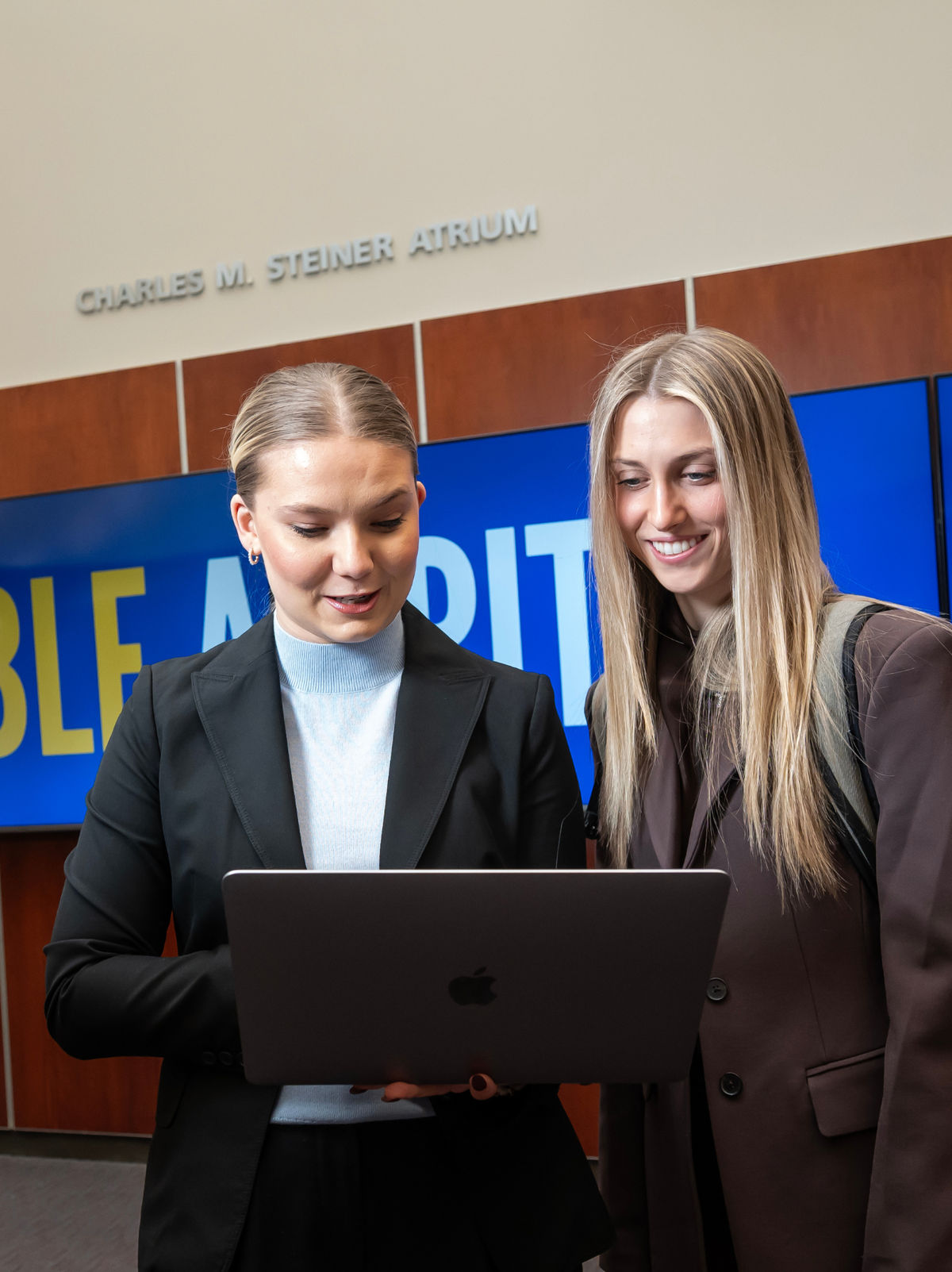 Two students looking at a laptop together in a university atrium.
