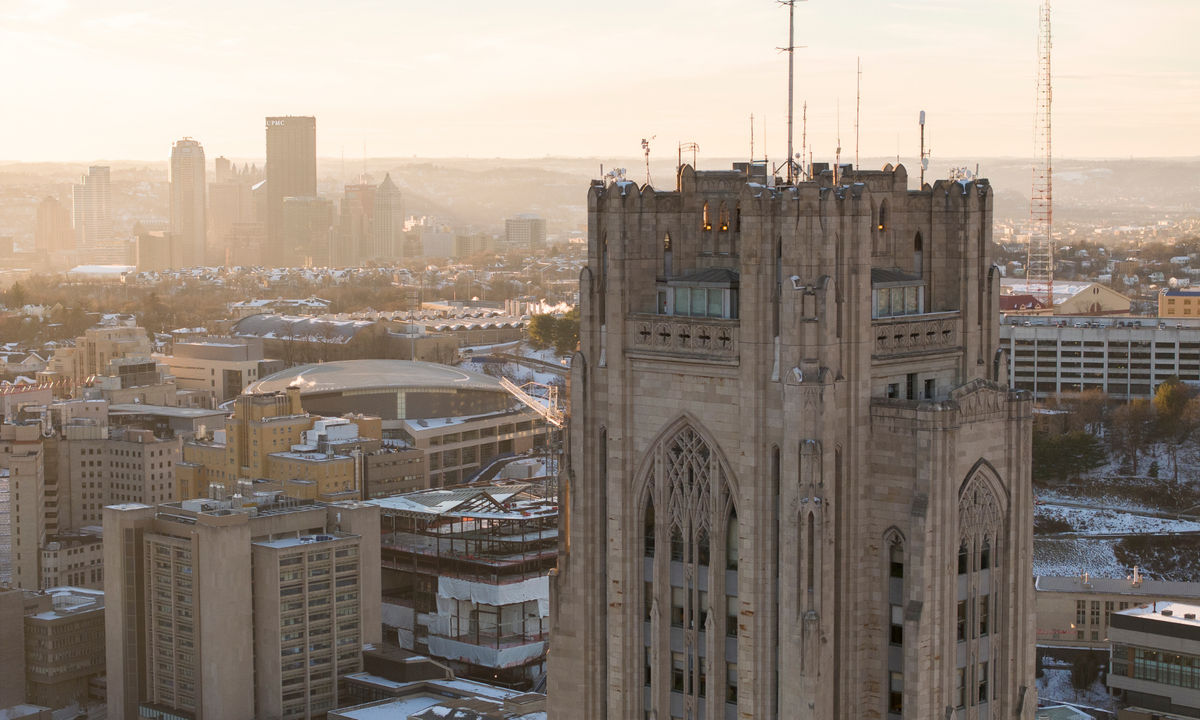 An aerial view of the Cathedral of Learning with the Pittsburgh skyline in the background.