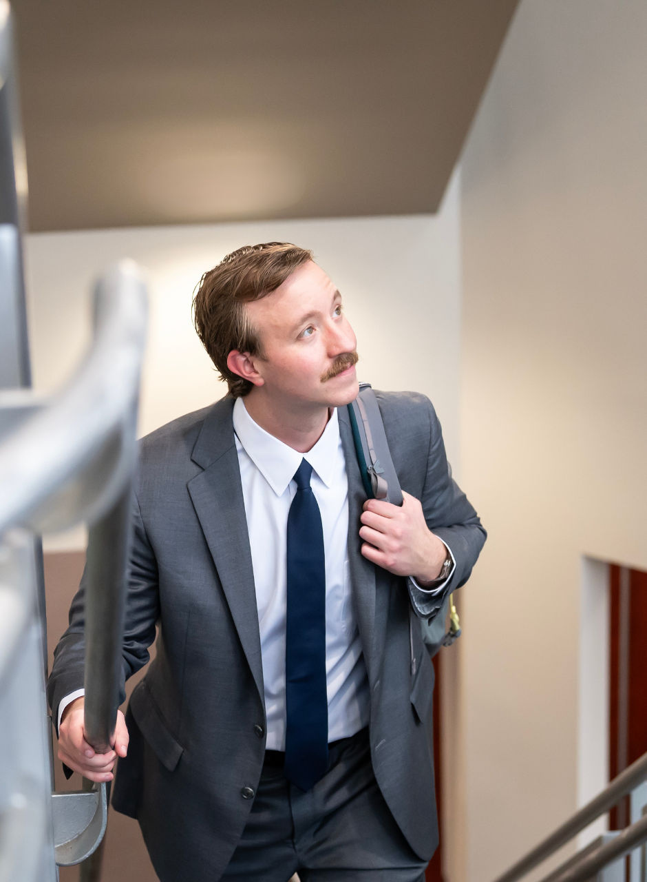 A person in a suit and tie carrying a backpack on a staircase.