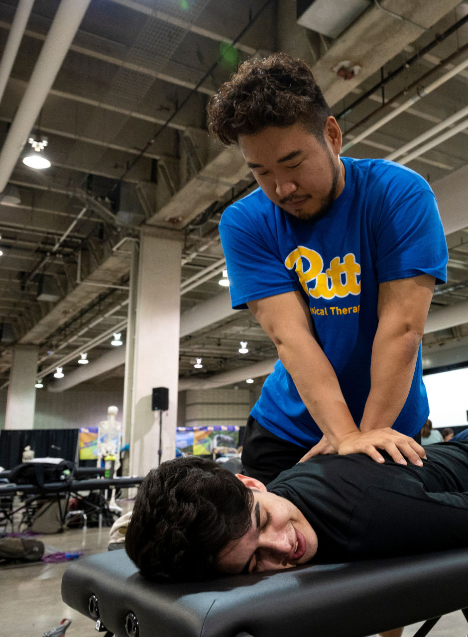 A physical therapy student practicing a hands-on technique on a person lying on a treatment table at a public event.