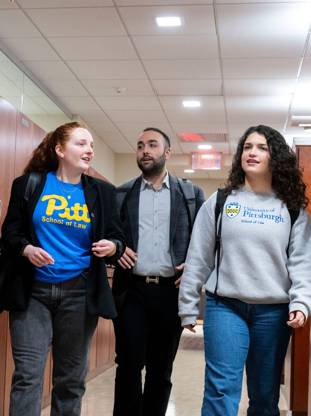 Three students walking and talking in a university hallway.