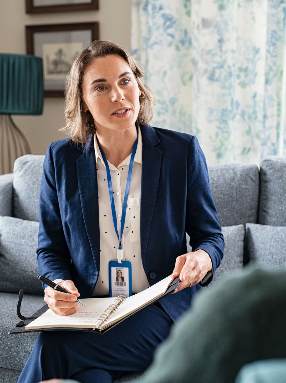 A professional wearing a badge and holding a notepad, speaking with someone.