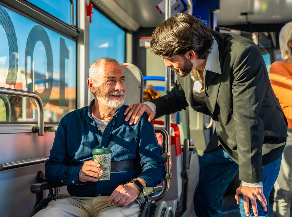 Two people having a friendly conversation on a bus, one seated in a wheelchair.