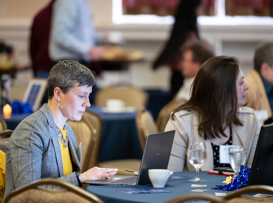 Two people working on laptops at a table during a conference or professional event.
