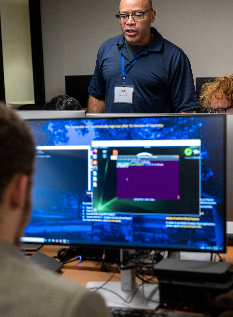 An instructor leading a session in a computer lab, with a monitor in the foreground displaying a software interface.