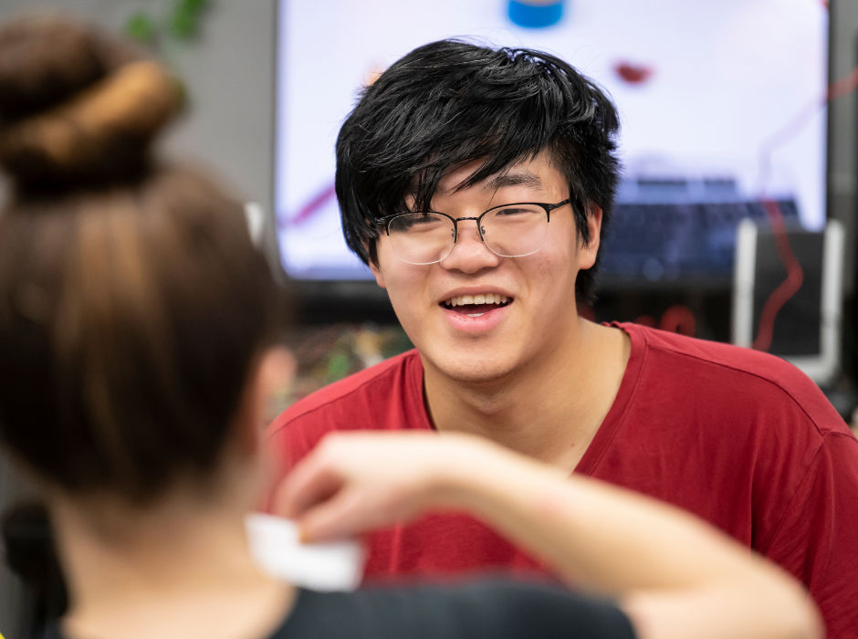 A smiling student talking with a classmate in a classroom setting.