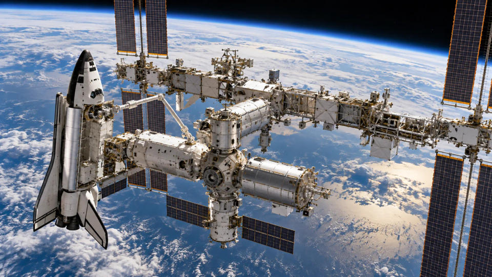 Partially assembled International Space Station with a space shuttle docked above Earth.