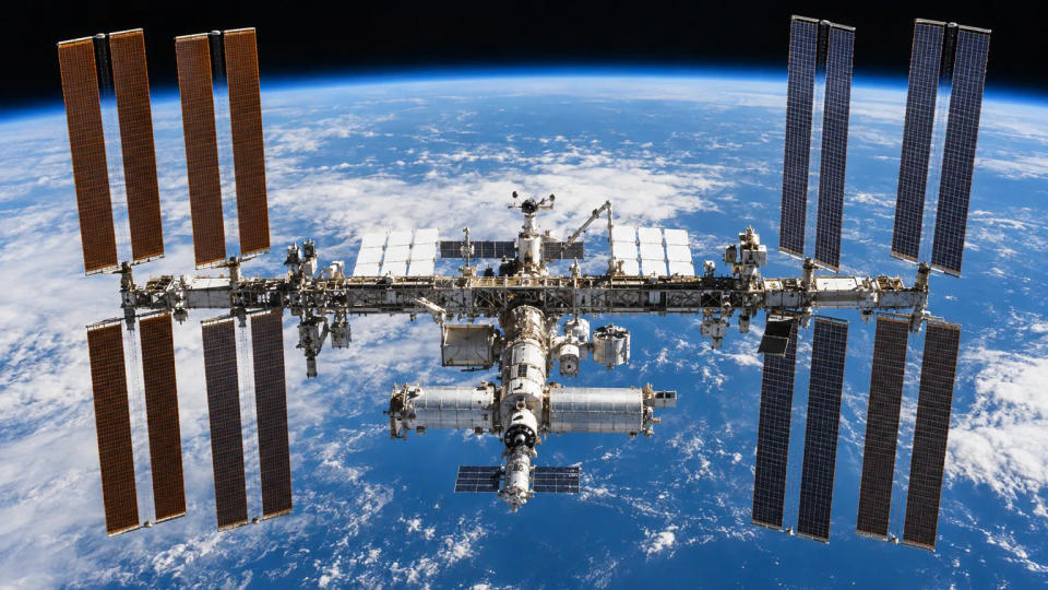 International Space Station above Earth with its long truss, radiators, modules, and multiple solar-array wings extended.