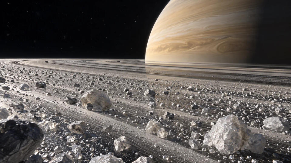 A close spacecraft-style view across countless icy particles and boulders in Saturn's thin rings, with Saturn beyond them.