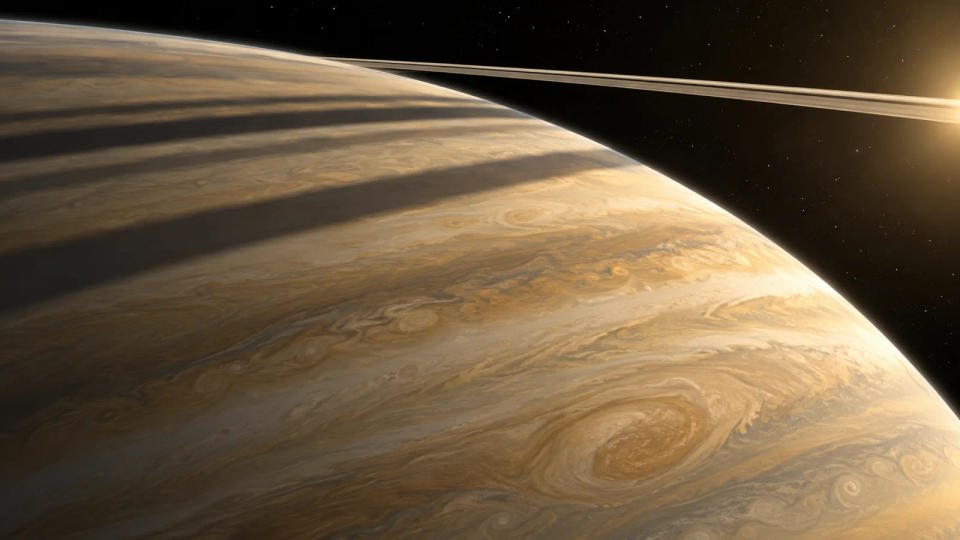 An orbital view of Saturn's golden cloud bands crossed by long dark shadows from the planet's thin rings.