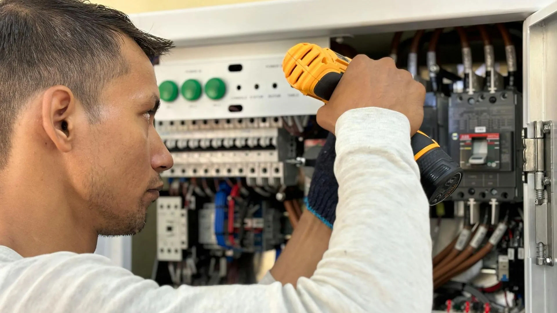 Professional electrician working on an electrical panel with a drill