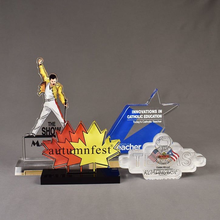 Four custom shaped Elite Series LaserCut™ Acrylic Awards showing a Market 58 trophy. Autumnfest trophy, Texas Roadhouse trophy and Catholic Teach trophy.