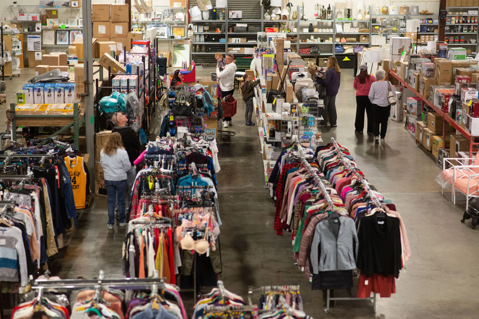 Shoppers in de gangpaden van een discountwinkel met rekken vol kleding en bazaar gekocht op buy-to-resell veilingen