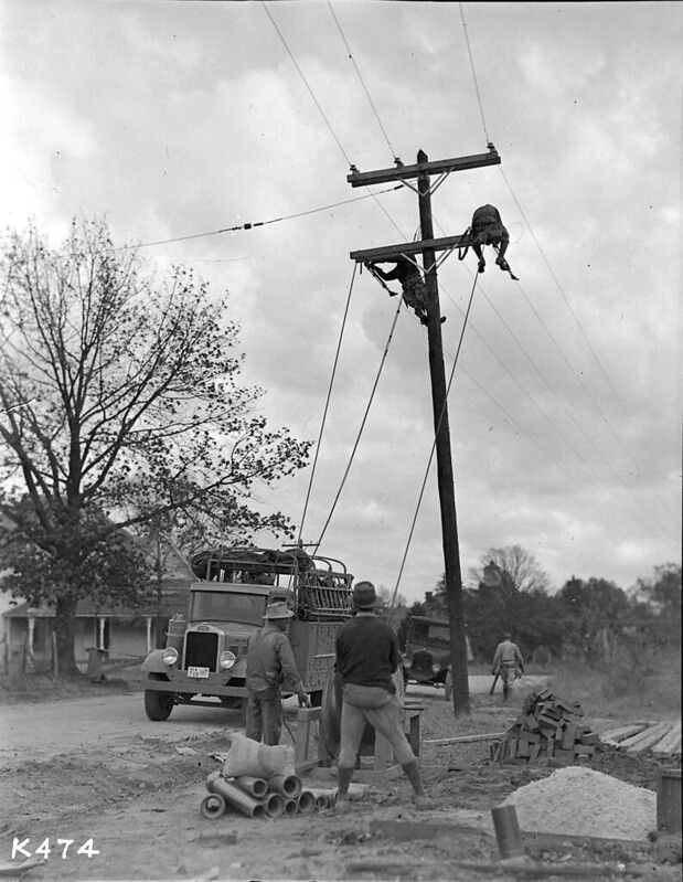 Workers repair telephone pole, truck nearby.
