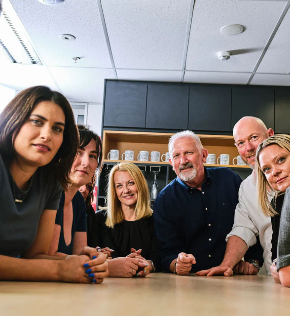 A group of people sitting around a table looking into the camera