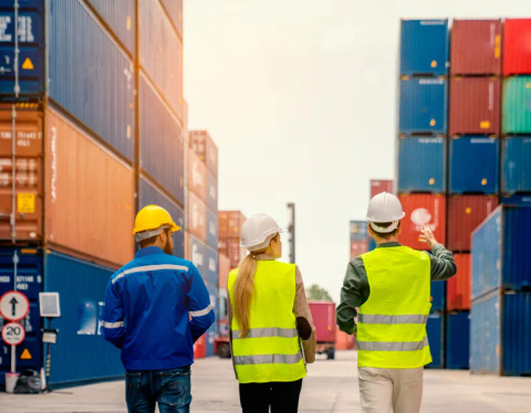 Three workers walking amongst stacked shipping containers.