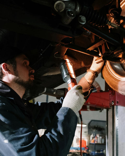 An auto mechanic standing underneath a car axle.