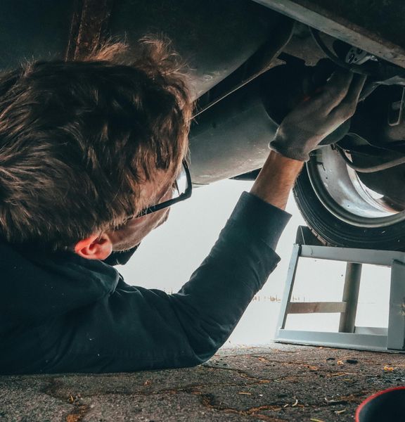 An auto mechanic underneath a car engine.