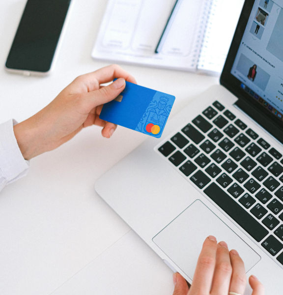 Hands holding up a credit card in front of a laptop.