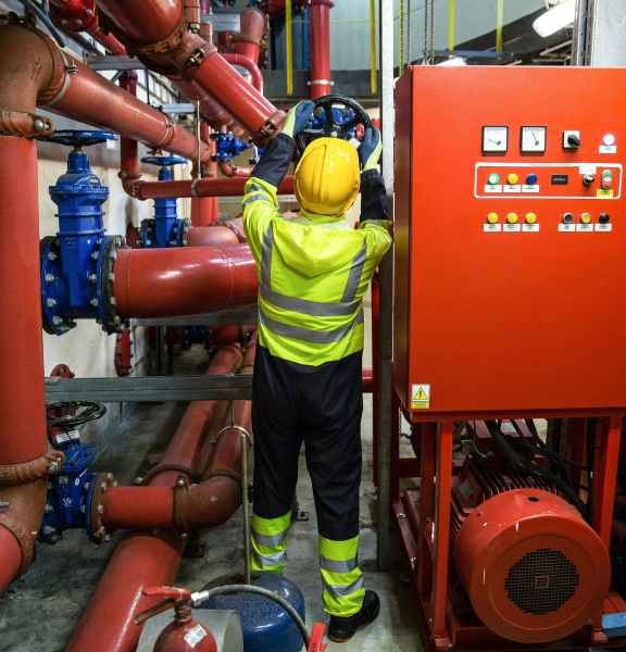 An image of a person in reflective high visibility clothing and a hard hat turning a large valve
