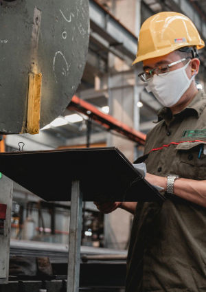 An image of a man wearing a hard hat and face mask looking at paperwork