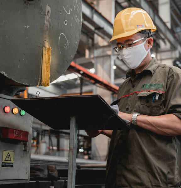 An image of a man wearing a hard hat and face mask looking at paperwork