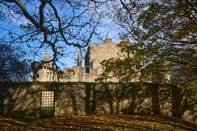 Craigmillar Castle. A peaceful stone cottage, surrounded by trees, with a charming window and wooden door. Serene and rustic ambiance.