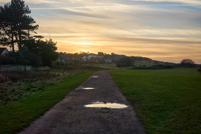 Gullane, East Lothian, Scotland. Sunset in the city: a meandering wet path reflects the evening sky, flanked by a grass field.