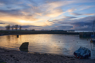 Port Seton at Night. A calm boat floats on a serene body of water, creating ripples that distort the reflection of the landscape.