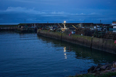 Port Seton at Night. A serene harbor scene with a dock, boats in calm waters, and reflections. Gently rippled water, clear sky, fluffy clouds - a peaceful atmosphere.