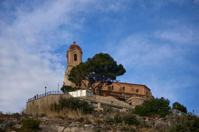 Castle of Cullera. A grand, majestic building with intricate details and a tower stands on a hill. A tree on the tower adds a touch of nature, harmonizing with the man-made structure.