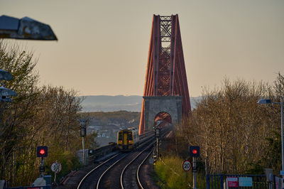 Train approaches the red Forth Bridge at dusk.