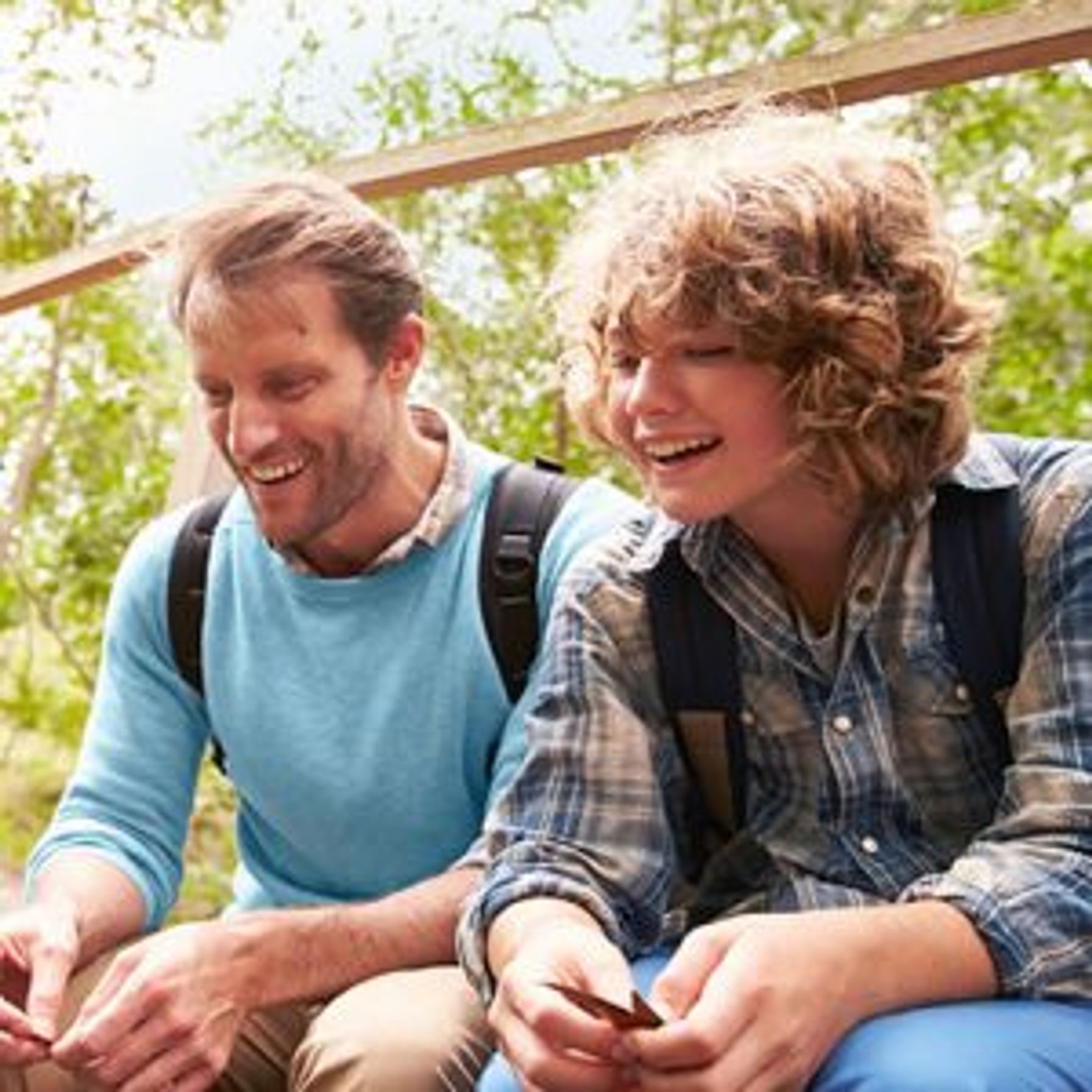 A father and son wearing backpacks, sitting outside