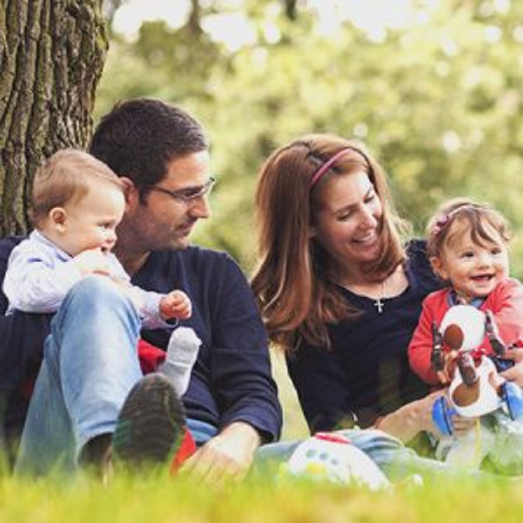 Two parents each holding a toddler sitting outside