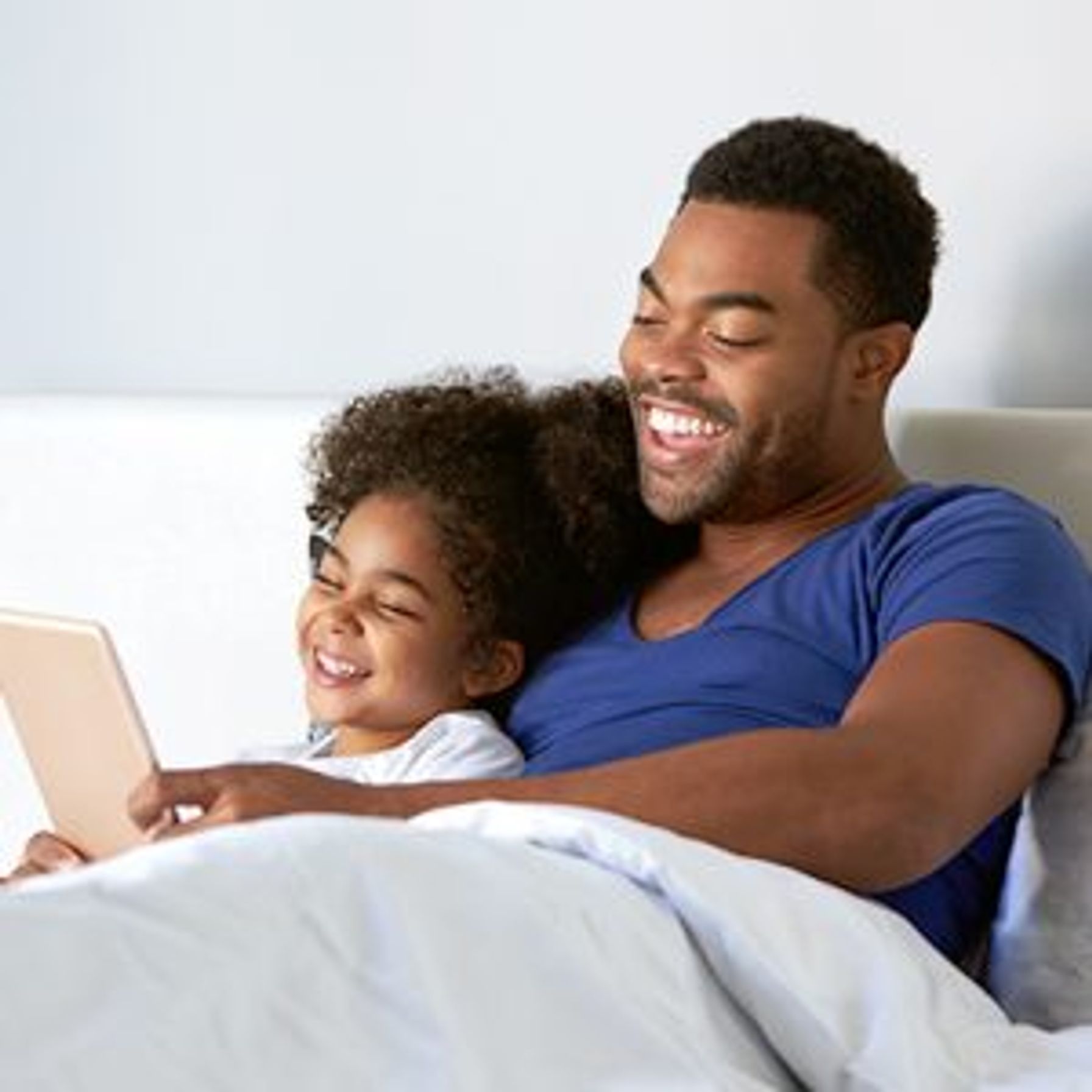 A dad laying in bed with his daughter watching Ipad