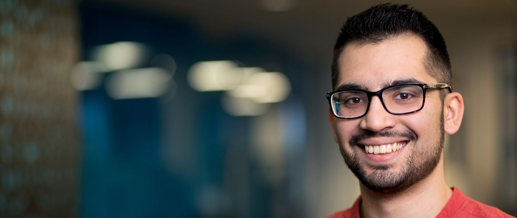 A portrait of a brunette man with glasses smiling