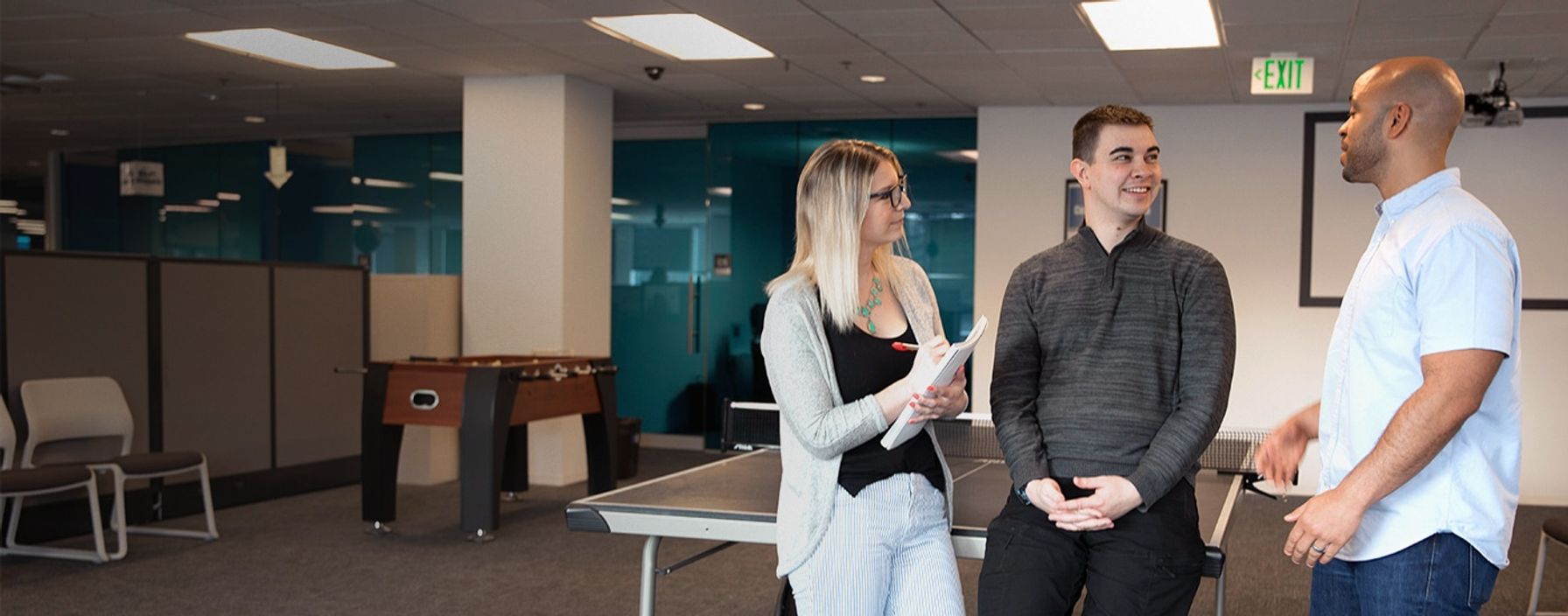 Two man and a woman talking near a ping-pong table