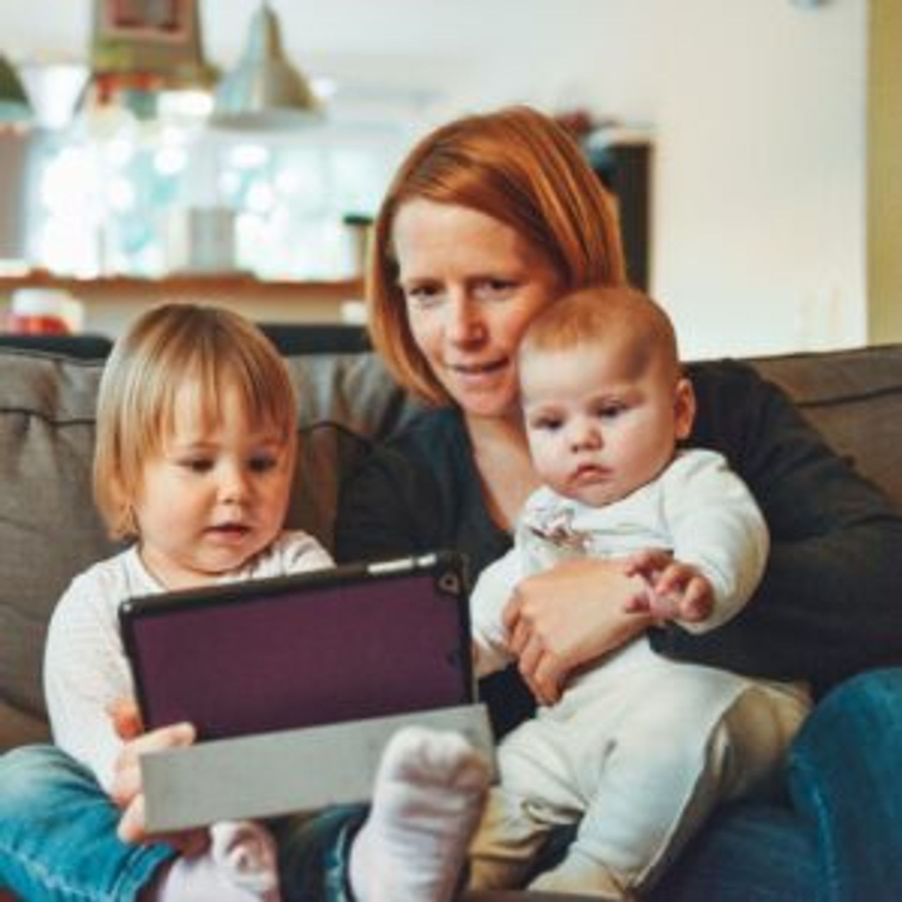 A mom watching an Ipad with her two young children