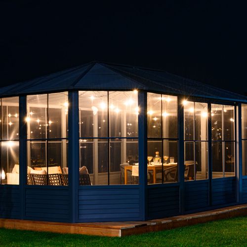 Elegant outdoor screened gazebo illuminated at night with cozy furniture and warm lighting.