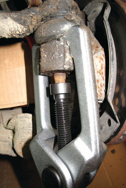 This puller’s twin arms grasp the top of the steering knuckle while its center bolt push- es upward against the tie-rod end’s rusty tapered stud.