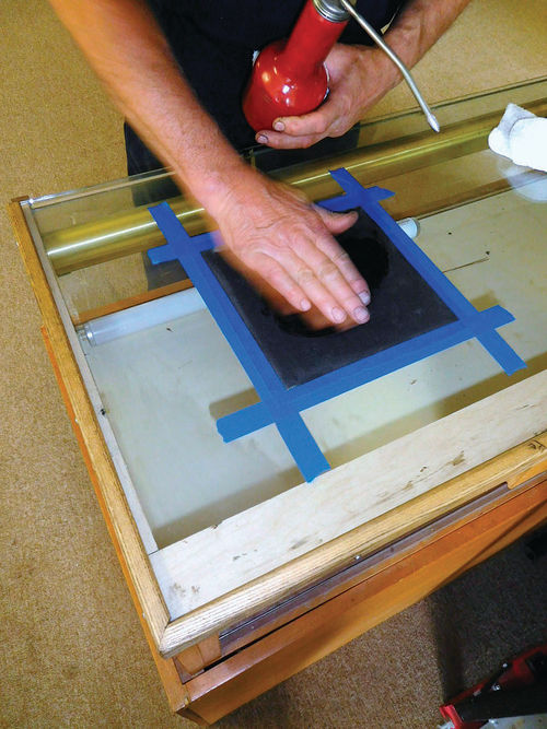 Dave Sarna checks with his hand to make sure the oiled sandpaper is slippery.