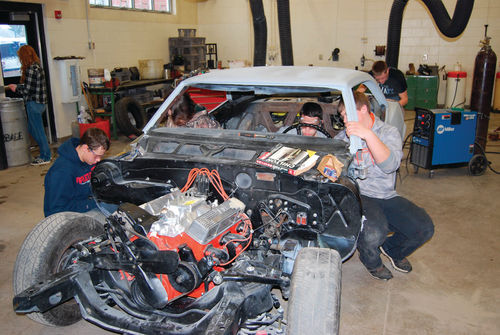 Joseph Landvatter crouches into the cockpit to give Isaiah Wentzel a hand adjusting the steering column. Meanwhile, Josh Peglow works on the passenger door hinge.