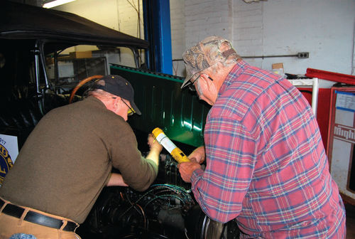 Bob Buchman holds the drop light while Dave Sarna tackles some engine adjustments.