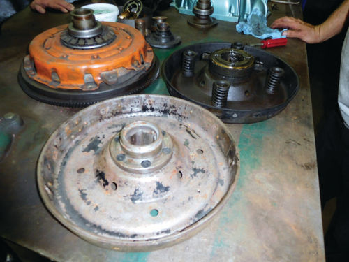 The orange clutch is a relatively modern one. The used demonstration clutch lined with brake material that we borrowed from Andy Wise is toward the camera. The old clutch is the dark, oily one with the coil springs and throw-out bearing still attached.