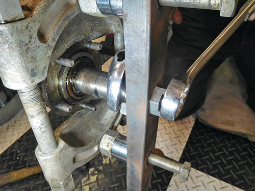 A long-handled, large-diameter wrench is used to turn the large axle nut to tighten it. Here the bearing pressed on the axle is just starting to come out of the axle housing.