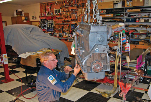 Auto technology instructor Dave Sarna bolts the oil pan onto a Chrysler straight eight that he lifted using a cherry picker hoist.